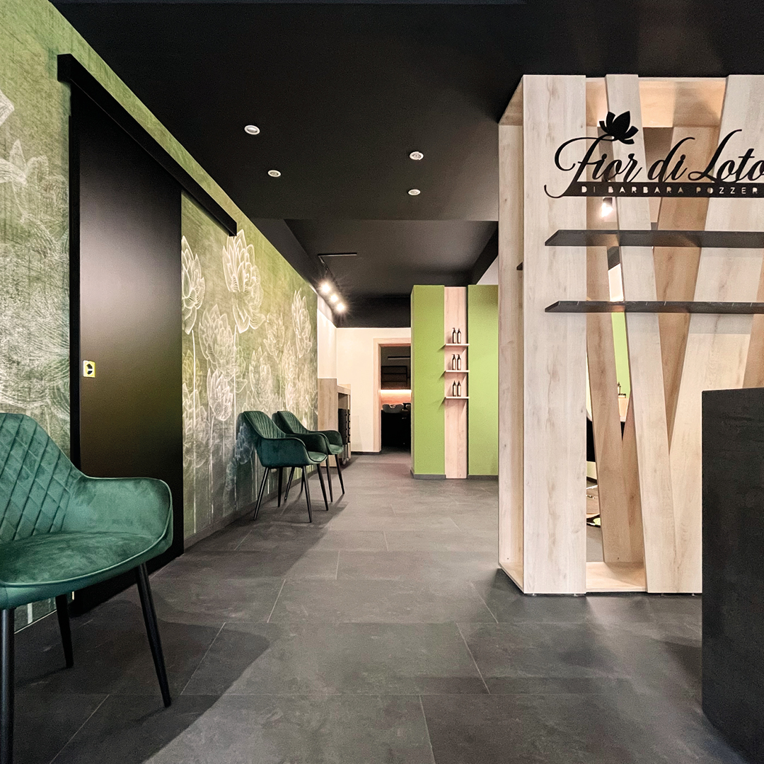 Immagine dell'area reception con pareti verde chiaro con motivi floreali bianchi. Poltrone verde scuro e mobilio in legno 
